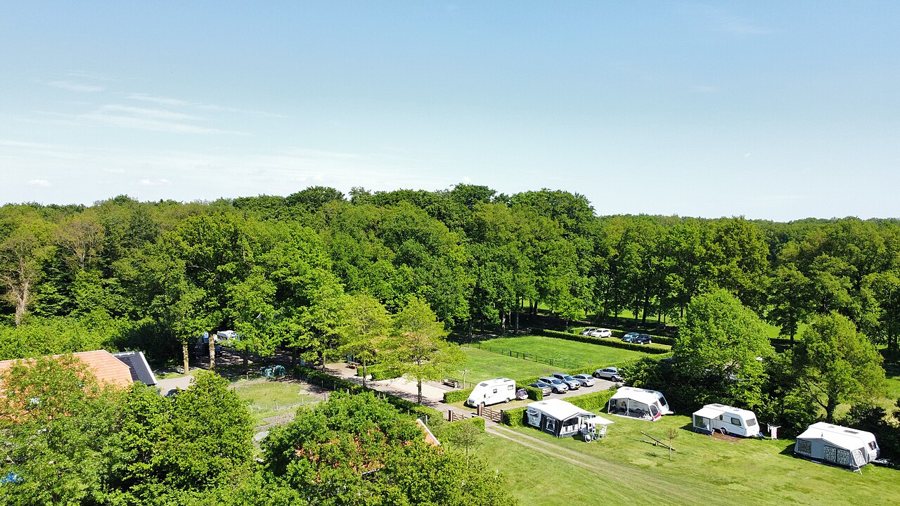 Luftaufnahme eines naturnahen Campingplatzes mit Stellplätzen und Wohnwagen