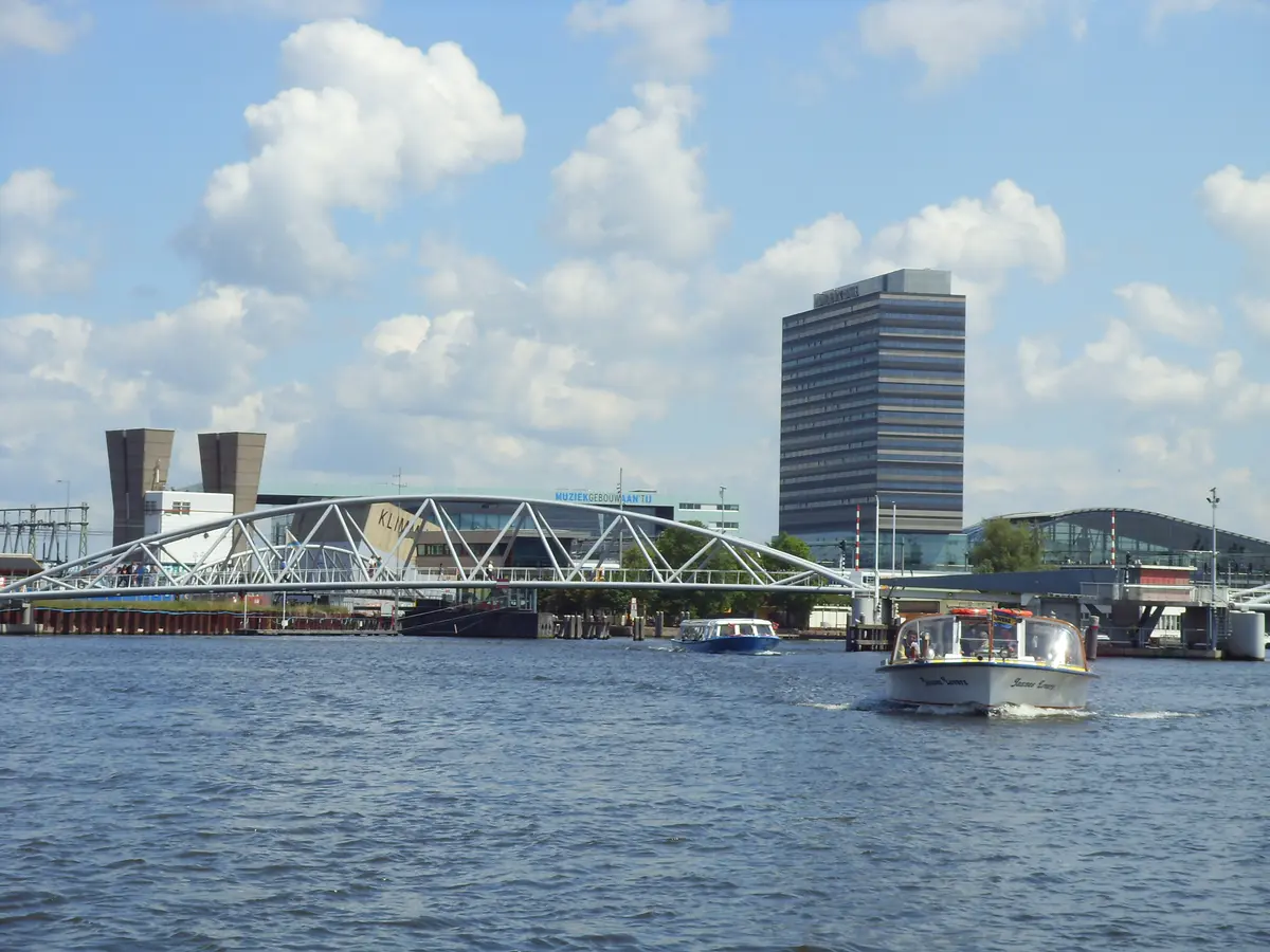 Ausflugsboote auf dem IJ vor einer Brücke und Gebäuden in Amsterdam
