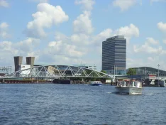 Ausflugsboote auf dem IJ vor einer Brücke und Gebäuden in Amsterdam